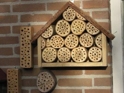 a solitary bee house on a wall, comprised of several segments of tree truck with holes drilled into them.