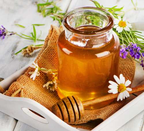 a jar of honey with a honey dipper on a tray with flowers