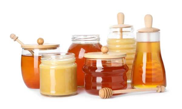 simple glass jar of honey with a wooden dipper, white background