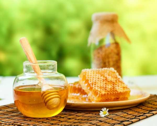 jar of clear honey with a honey dipper on a rattan place mat