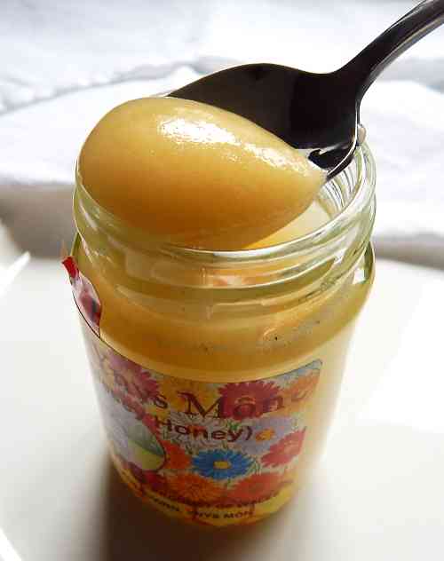 Honey, like many foods we commonly eat, is acidic. a jar of golden soft set honey, with a silver teaspoon just lifted out of it, and with honey on the spoon.